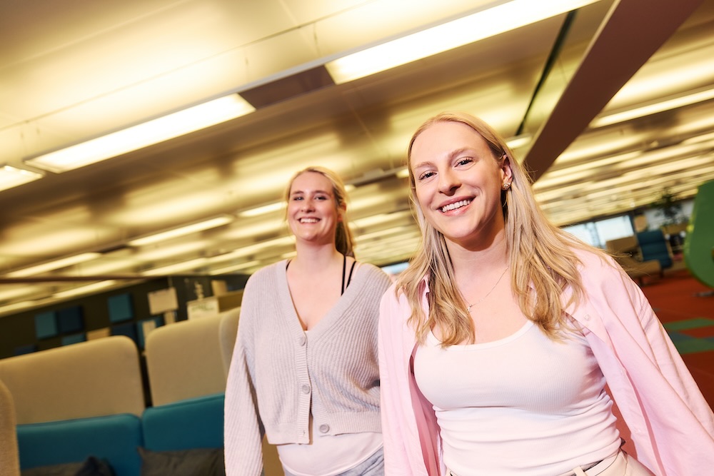 Zwei Studierende gehen lachend durch ein hell beleuchtetes und modern eingerichtetes DRV-Bund Gebäude.