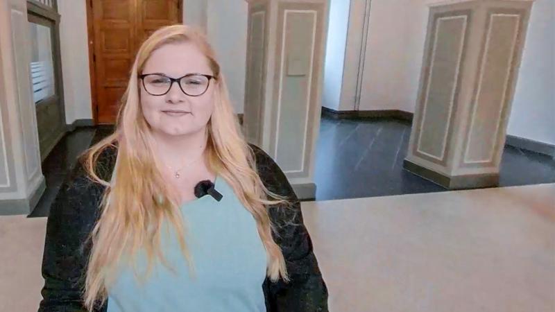 Duale Studentin mit langem blonden Haaren steht in einem Flur der DRV Bund, in dem zwei Säulen stehen.