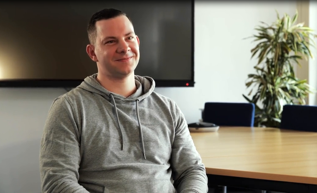 Mann sitzt lächelnd auf Stuhl.