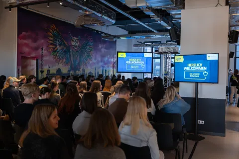 Blik auf eine Bühne, davor sitzen Menschen, sie sind nur von hinten zu sehen.